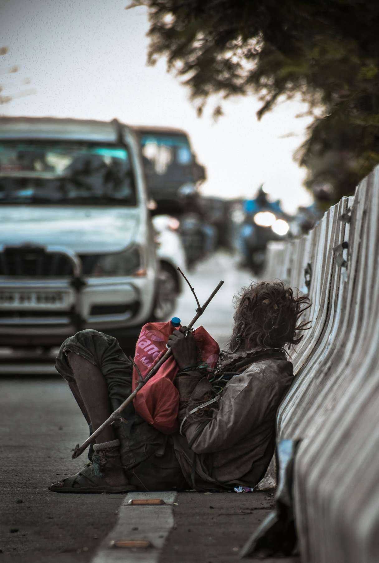 Man Sitting at the Side of the Road Leaning Back on Road Railing Near Cars during Day